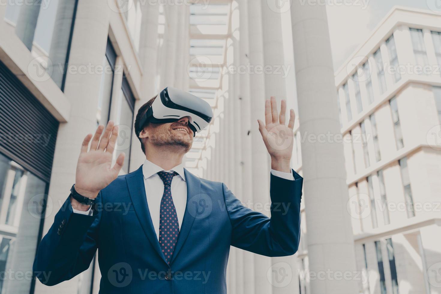 Young modern businessman in VR goggles on head working in augmented reality world and smiling photo