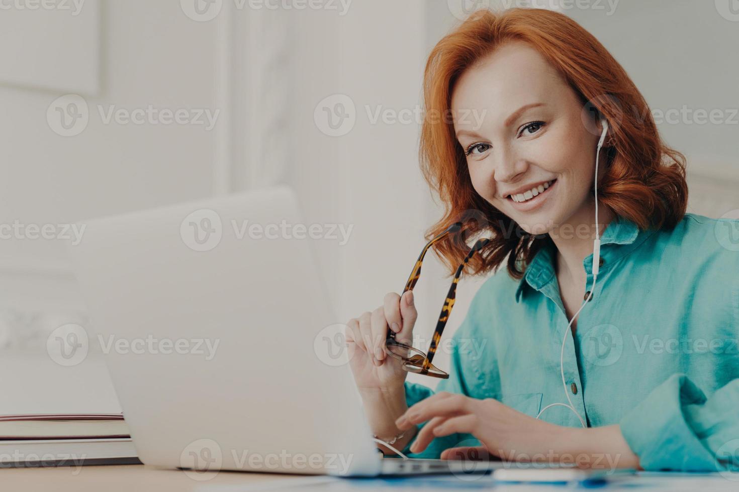 Smiling good looking female employee talks on video call, has web conference with colleagues, watches webinar on modern laptop, poses in coworking space. Student learns foreign languages online photo