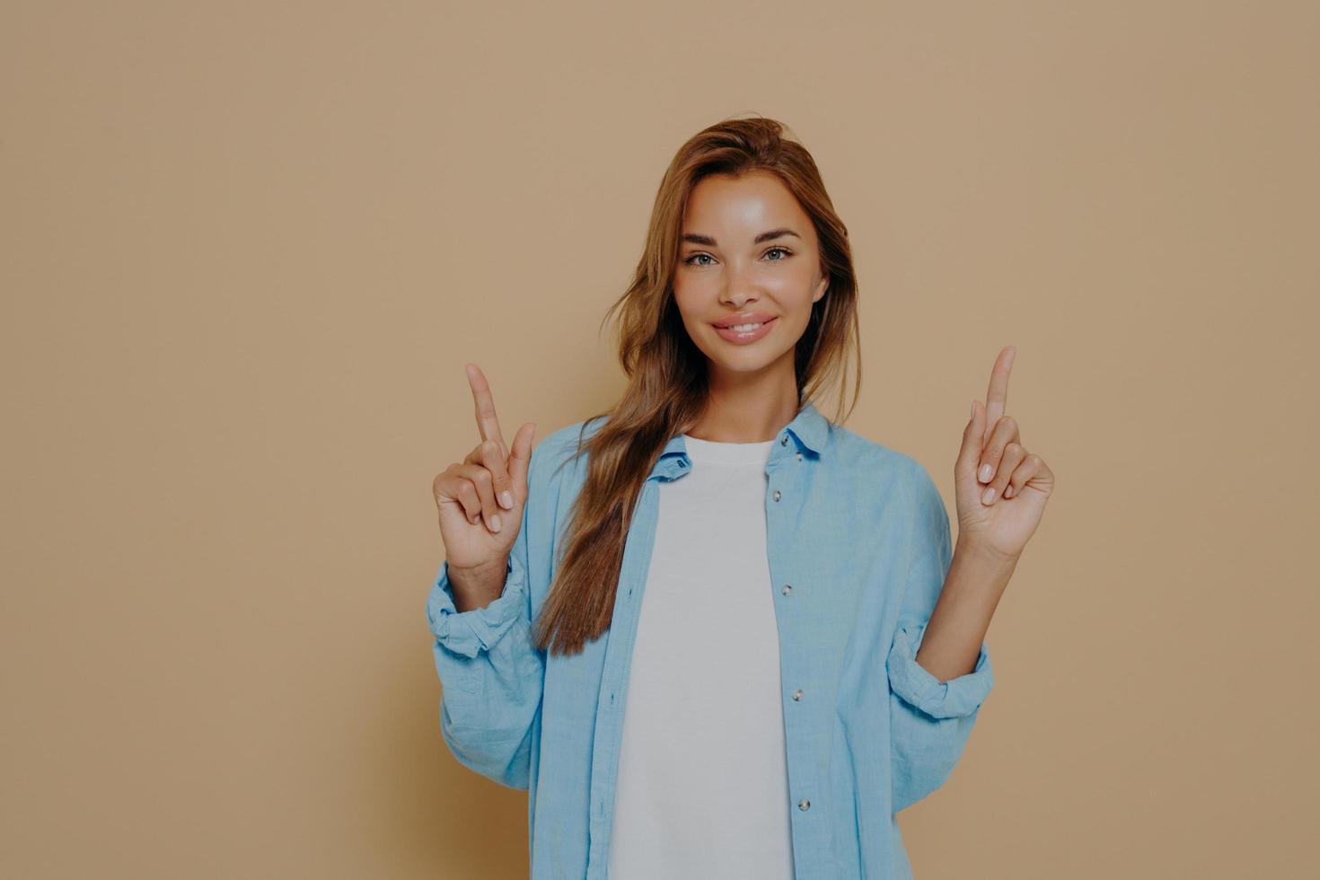 Excited cheerful european female with long brunette hair wearing casual clothes posing in studio photo