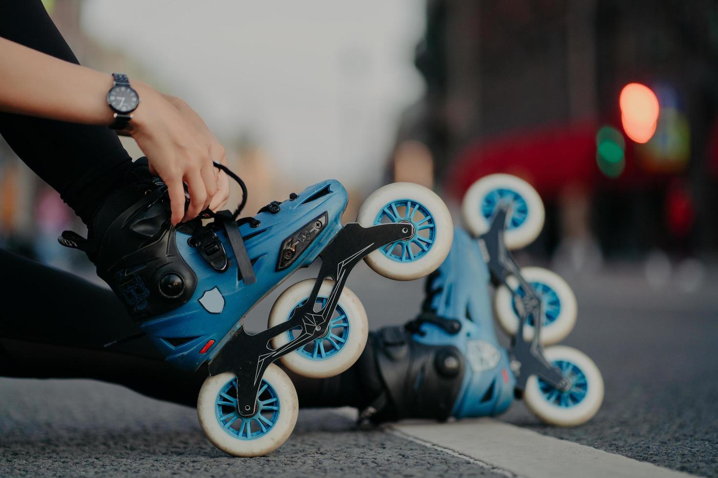 Cropped shot of unrecognizable woman puts on rollerblades poses outdoors on asphalt against blurred background. Unknown person wears rollerskates spends free time actively tries new purchase photo