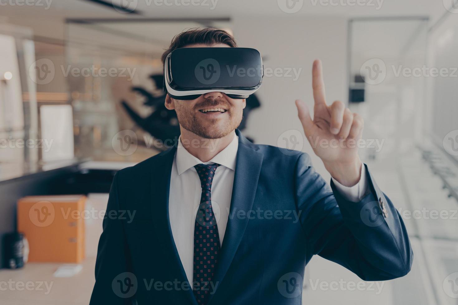 Young successful businessman in VR goggles touching air with finger during virtual business meeting photo