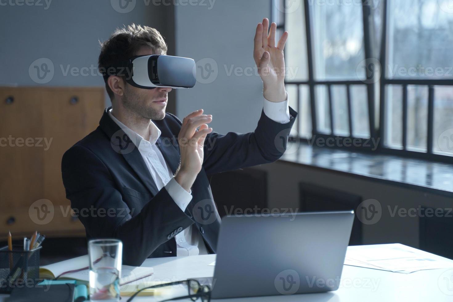 Male office worker in vr headset interacting with digital interface while sitting at desk photo