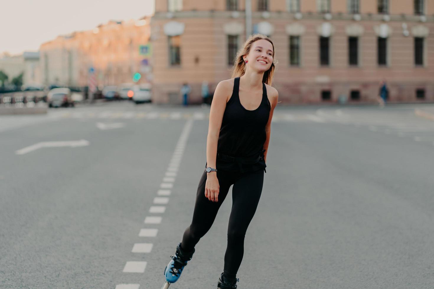 Healthy lifestyle summer leisure active outdoor recreation concept. Smiling dark haired young woman enjoys rollerblading as hobby looks into distance wears sportsclothes rides fast on rollers photo