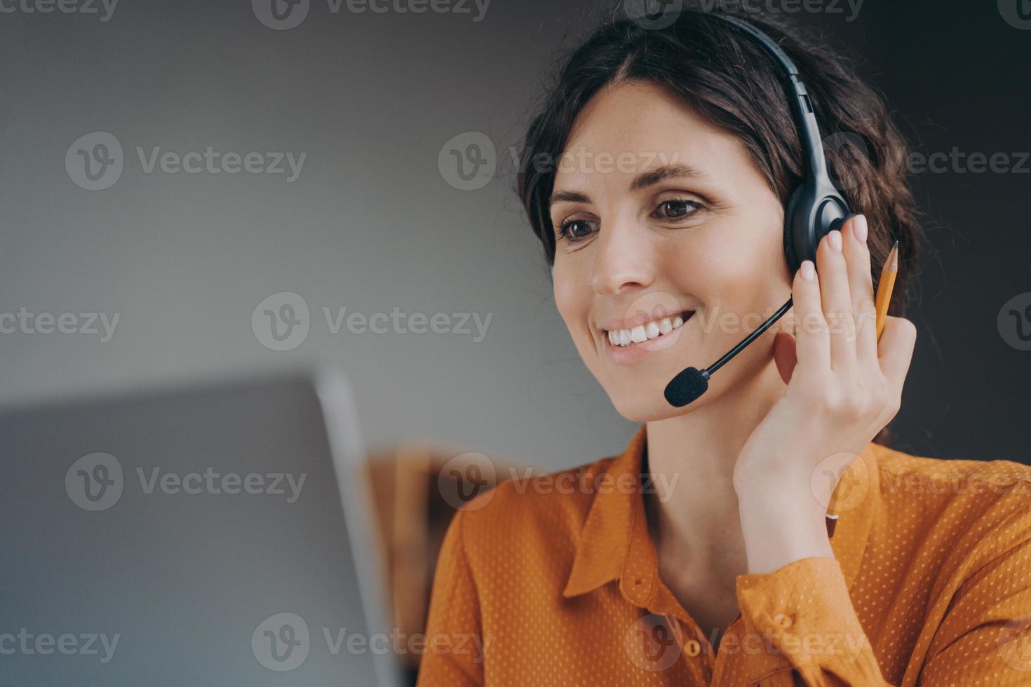 Pleasant woman Spanish speaking call center employee in wireless headset talking with client photo