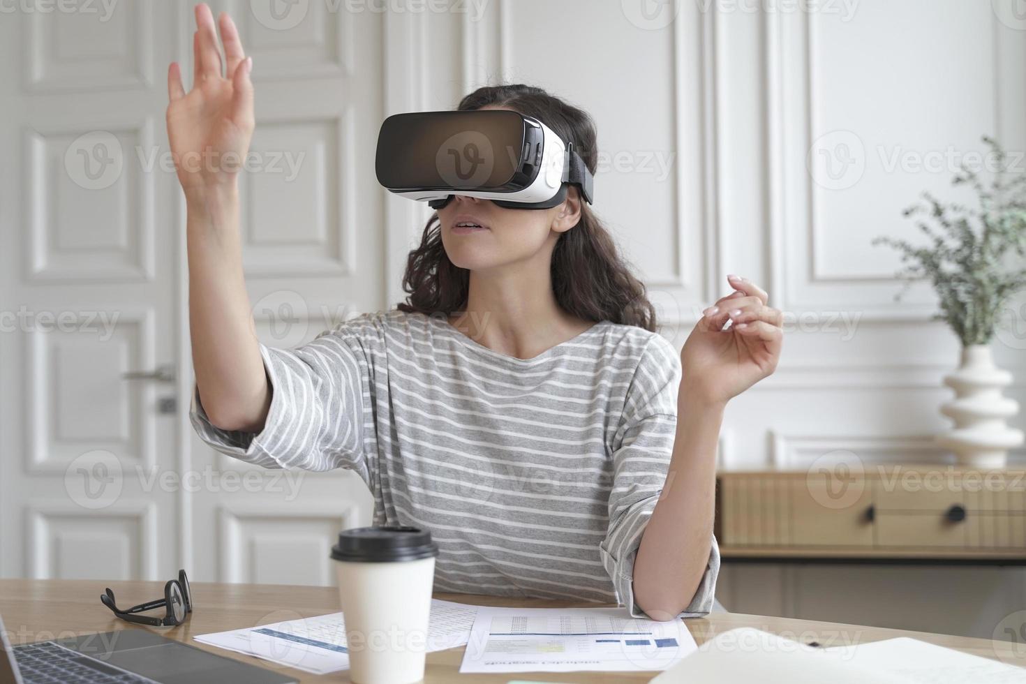 Concentrated woman bank accountant in VR headset sitting at desk at home office photo