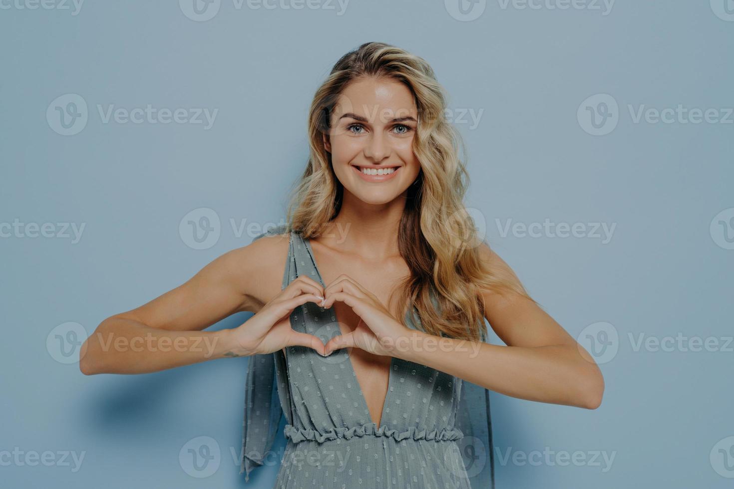 mujer encantadora feliz con el pelo largo rubio que muestra el símbolo del amor con las manos ahuecadas en forma de corazón foto