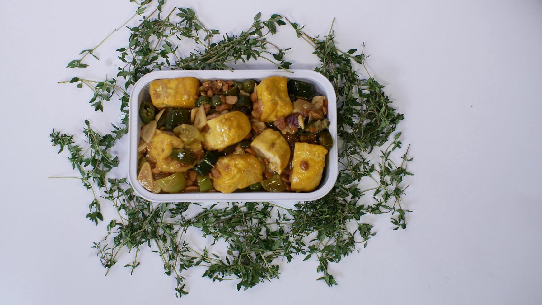 Vegetable tofu with yellow spices Indonesian food served in an aluminum holder with a white background with a few green leaves around it photo