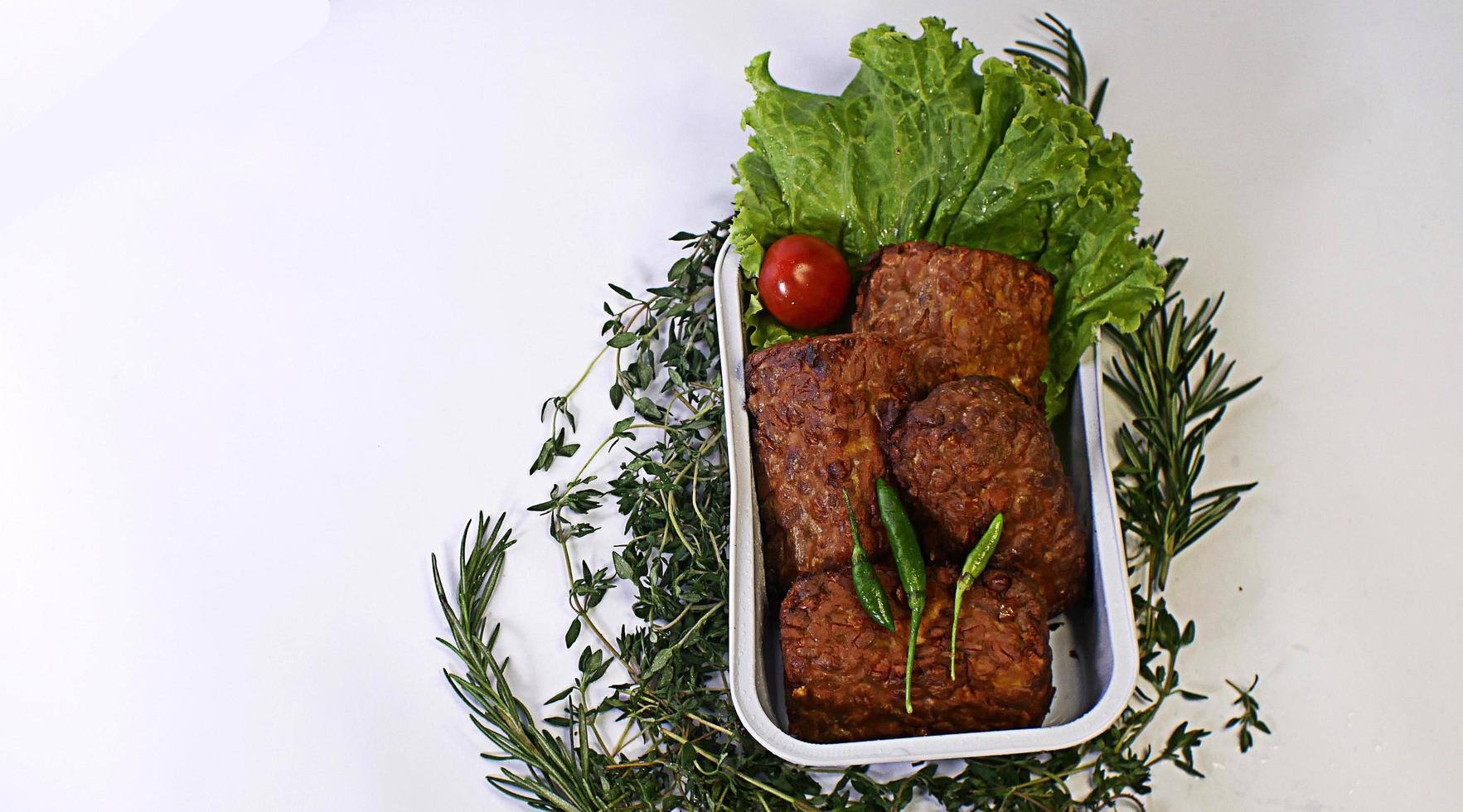 champiñones de soja fritos, tomates pequeños, chiles y ensalada en un recipiente de aluminio. típica comida callejera indonesia de fondo blanco foto