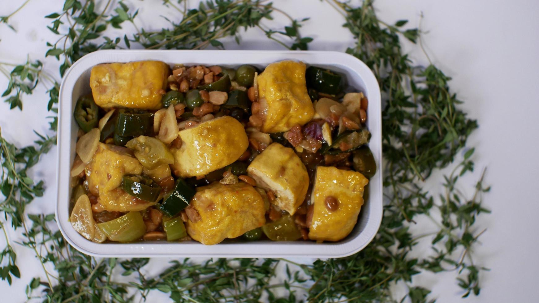 Vegetable tofu with yellow spices Indonesian food served in an aluminum holder with a white background with a few green leaves around it photo