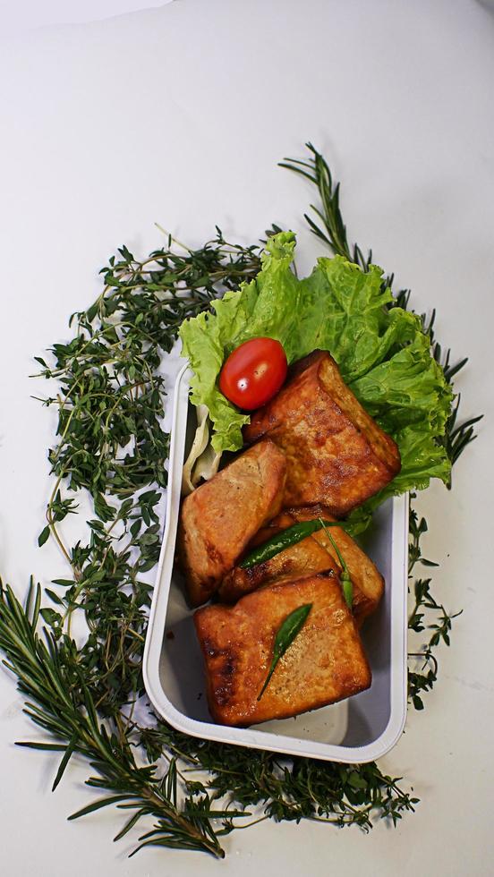 Fried tofu, small tomatoes and green chilies along with lettuce in one aluminum container, Indonesian street food on a white background photo