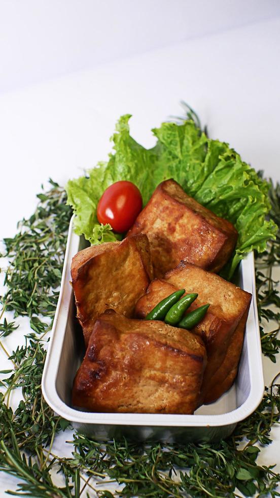 Fried tofu, small tomatoes and green chilies along with lettuce in one aluminum container, Indonesian street food on a white background photo