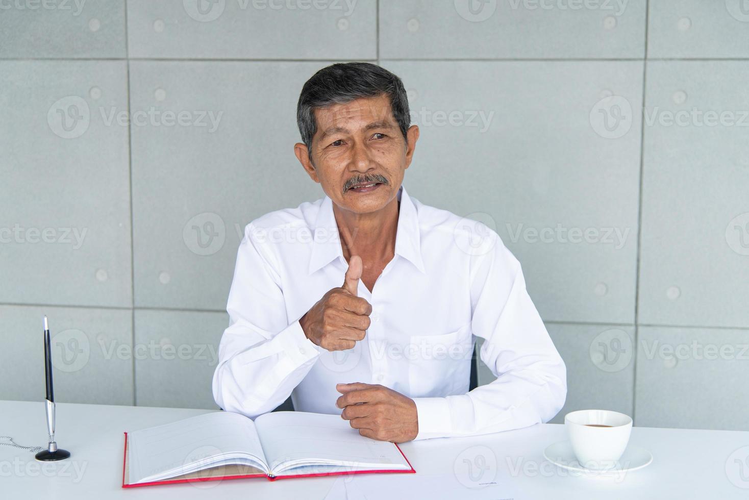 Work from home and social distancing concept. Asian business old man  working at co-working space or meeting room. Aging man sign signature and thumbs up. photo