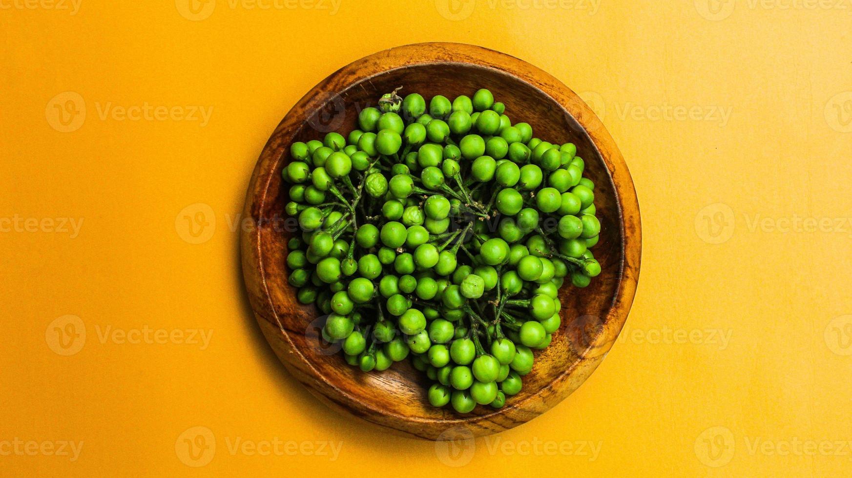 Takokak, Solanum Torvum, on wooden plate isolated orange background. Takokak fruit or sparrow eggplant is a plant from the eggplant tribe. Usually the fruit or seeds are used for fresh vegetables photo