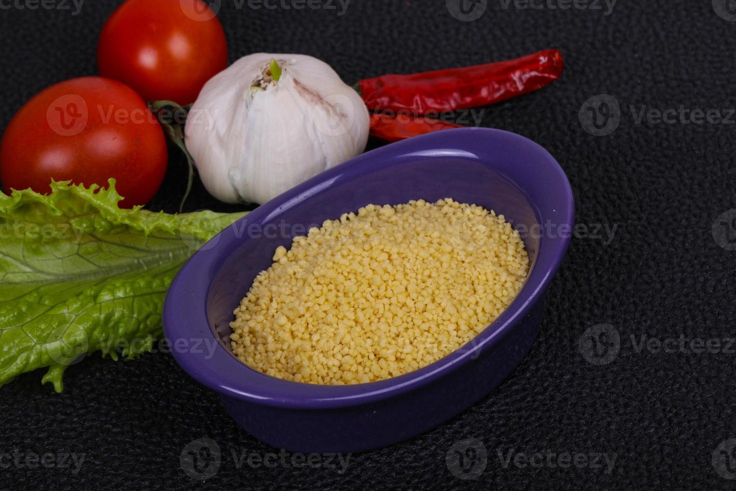 cuscús crudo en el bol servido con hojas de ensalada, tomate y pimiento foto