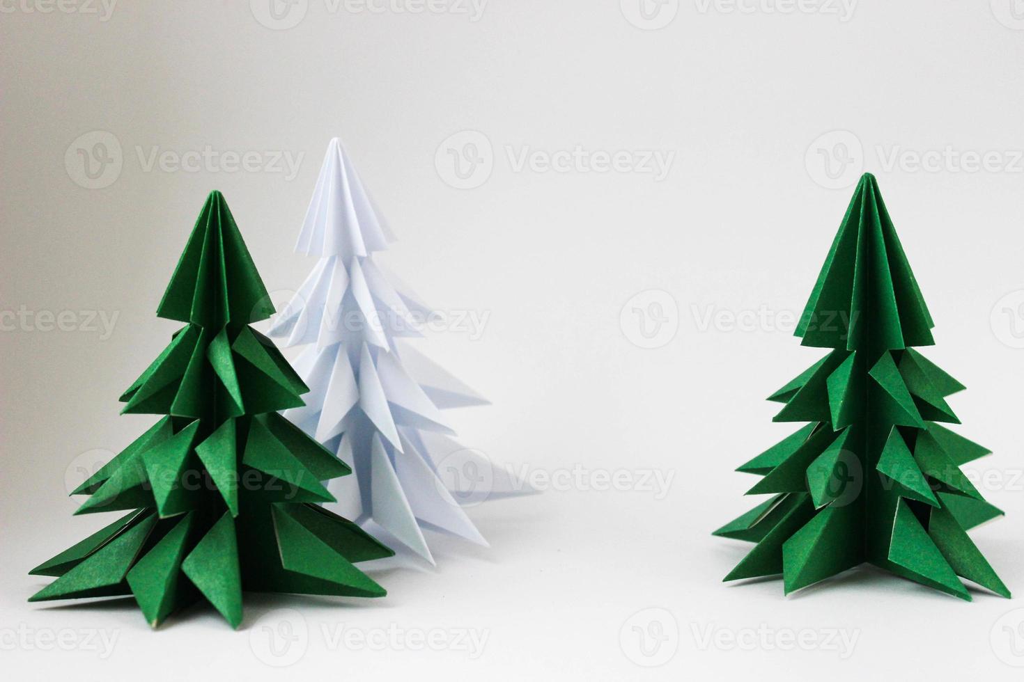 Two origami green christmas tree and white one on white background. photo