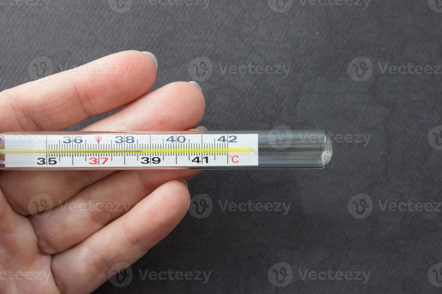 Mercury thermometer in hand on black background. Close up photo. Thermometer shows a temperature of 38.7 degrees Celsius photo