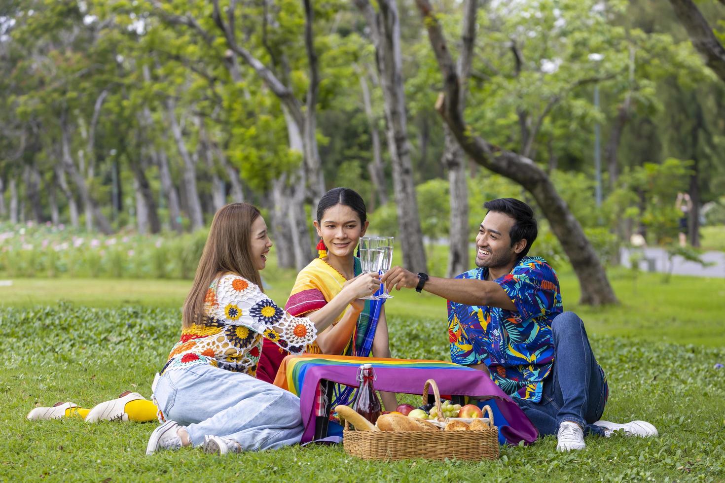 Group of transgender and homosexual people cheers and celebrating LGBTQ pride month in colorful dress and rainbow flag while picnic in the park photo