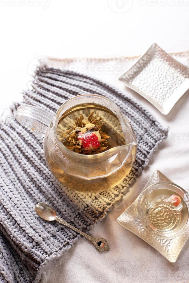 Exotic Green Tea Glass Teapot with Floral Blooming Tea Ball on White Table photo