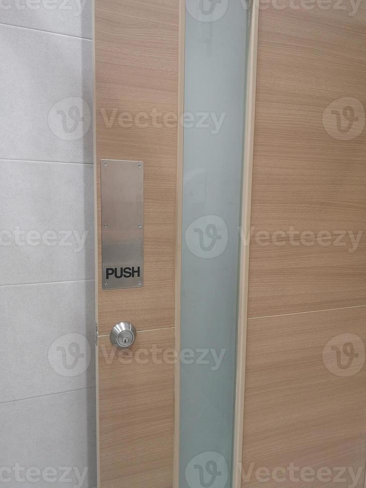 Push type door handle, black text latch in the stainless steel plate and keyhole on wooden door photo