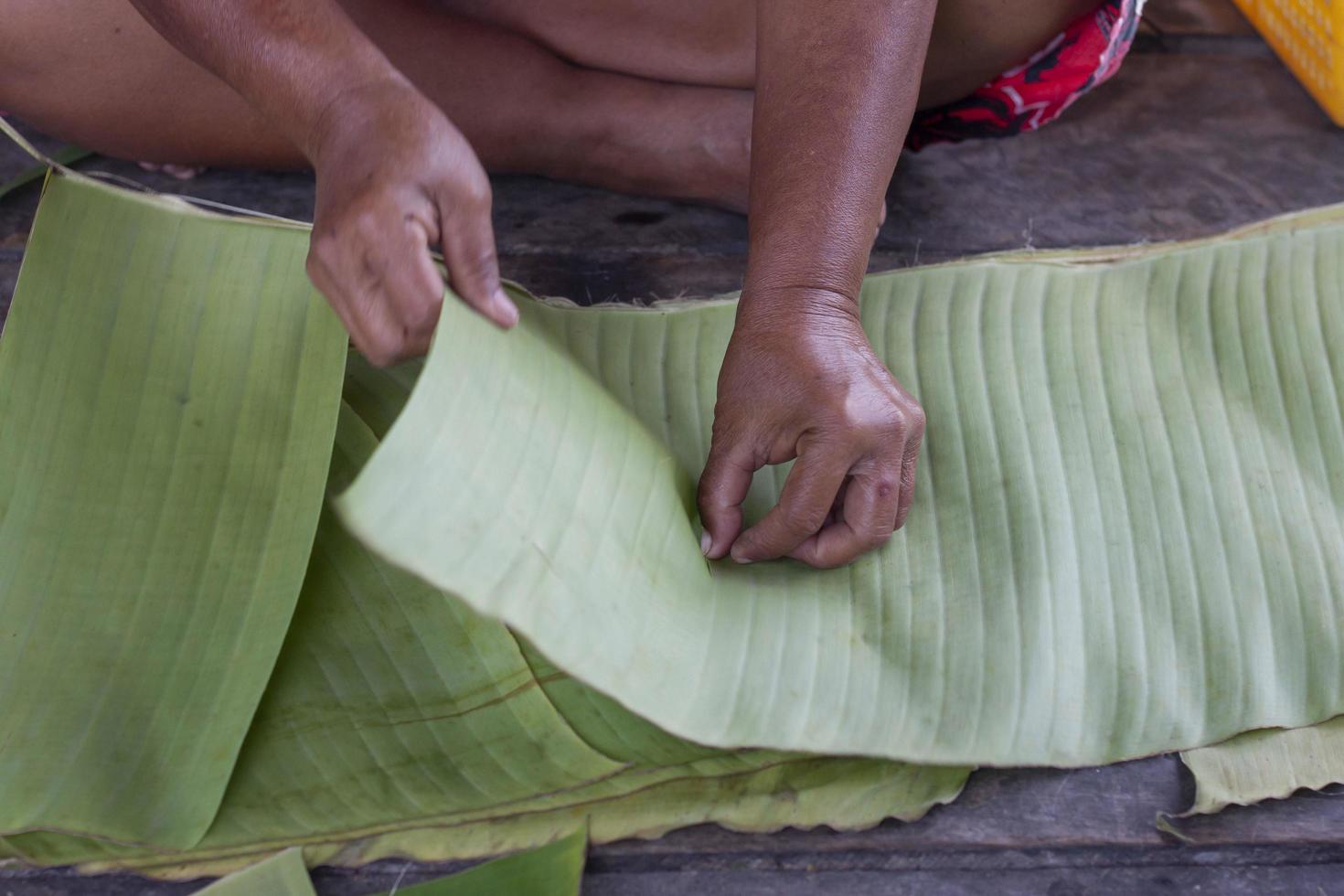 Hand of elderly woman sitting and tearing banana leaves to prepare for use as a container for food. photo