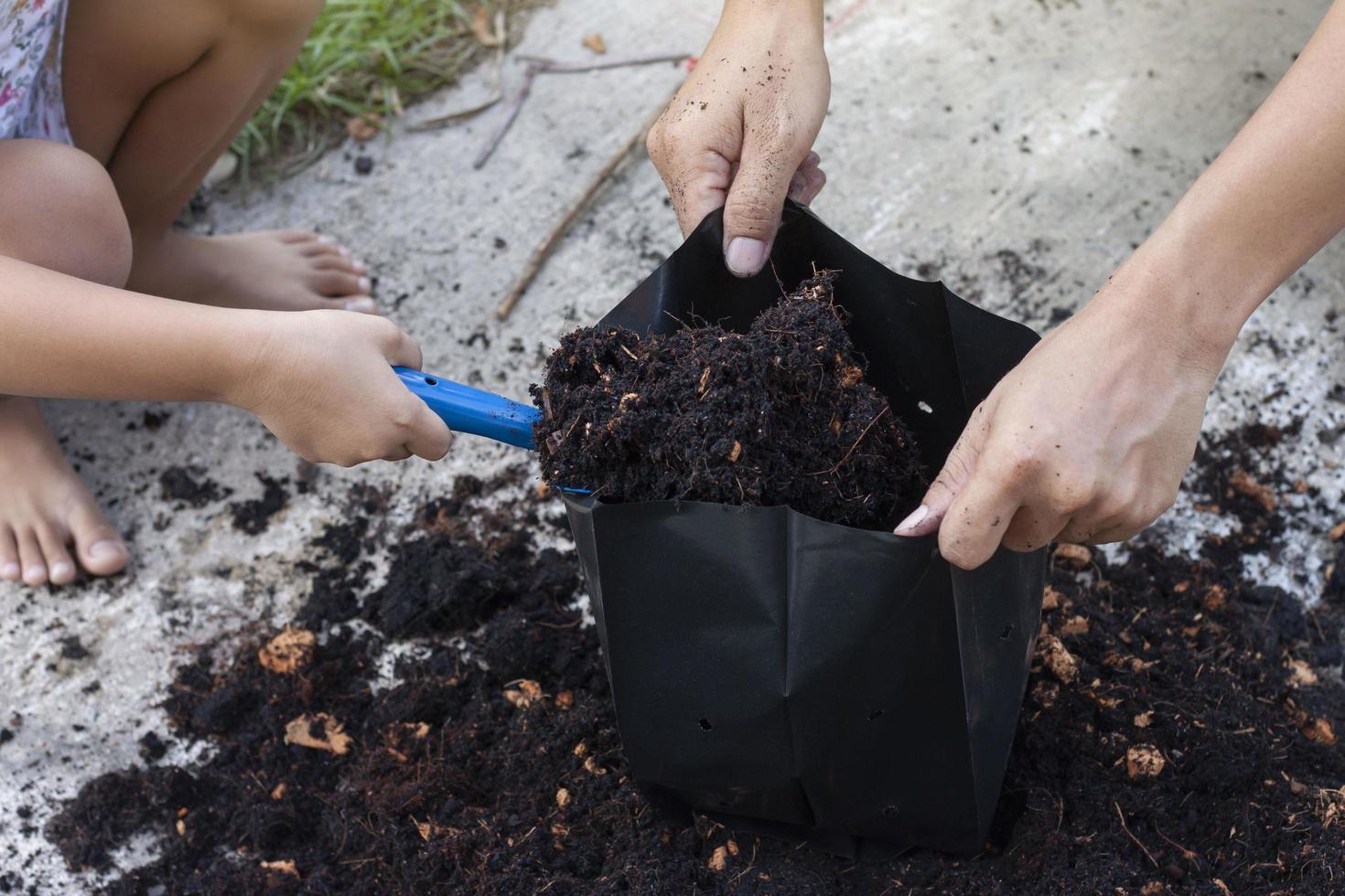 Hand of daughter holding a shovel to help father scoop up soil mixed with coconut dust put in a black plastic bag for nursery. photo