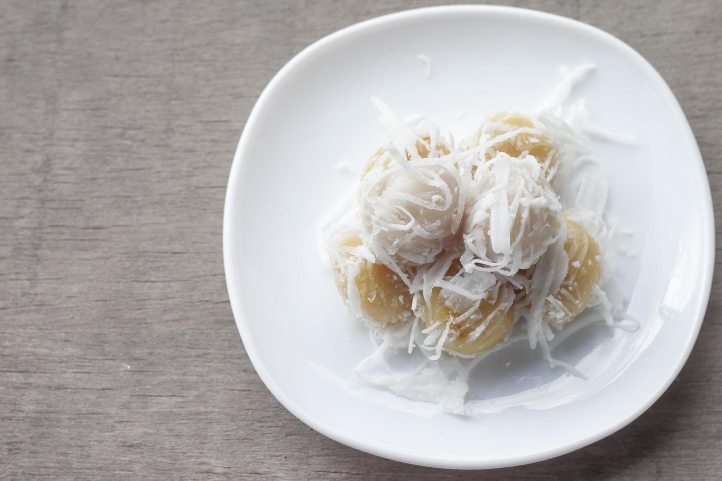 khanom tom kao es un postre tradicional tailandés de dulces hervidos en un plato blanco sobre una mesa de madera. foto