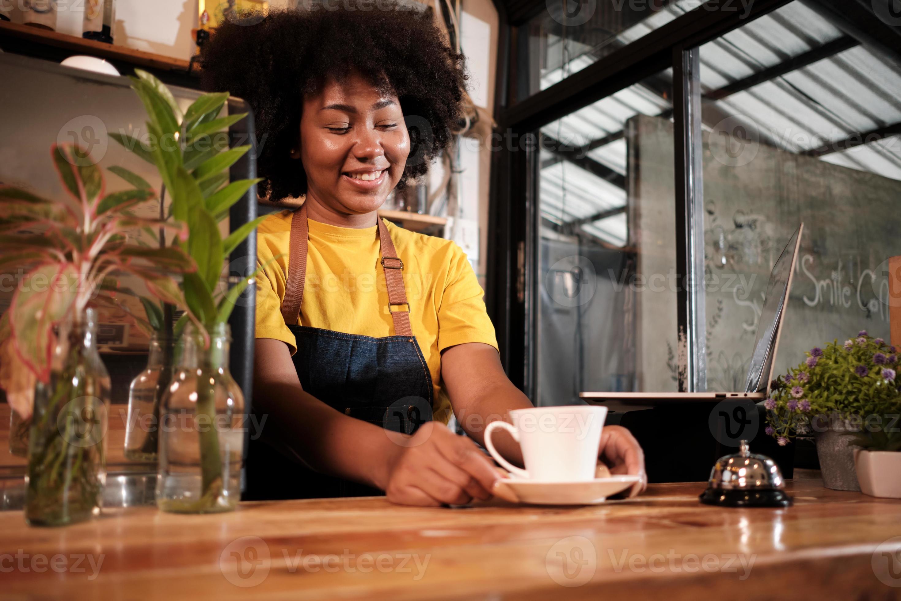 African American female barista offers cup of coffee to customer with
