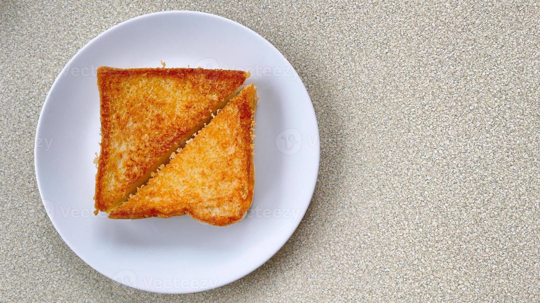 Two piece triangle slices of toasted bread made from white wheat flour and a slice of cheddar cheese in white plate. photo