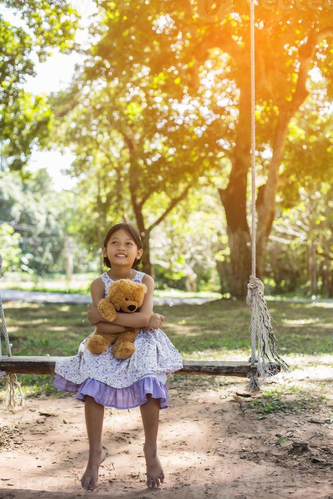 Cute little girl sitting swings , teddy bear sitting with her,little girl pointed to the tree. photo