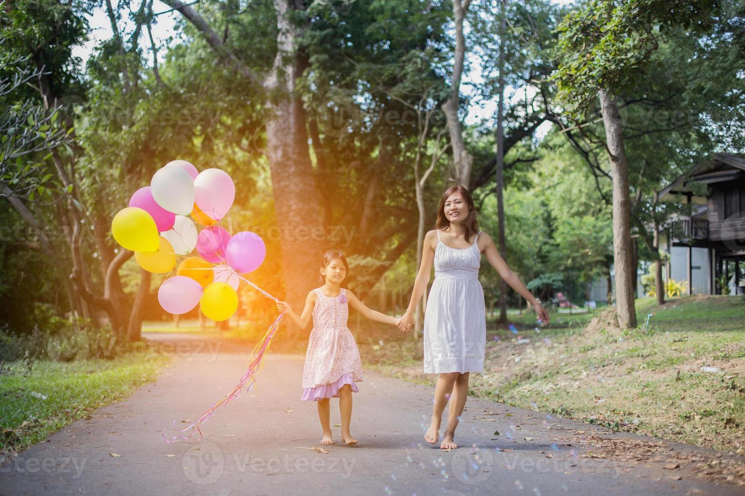 Cute little girl holding colorful balloons, running in the meadow against blue sky and clouds. photo