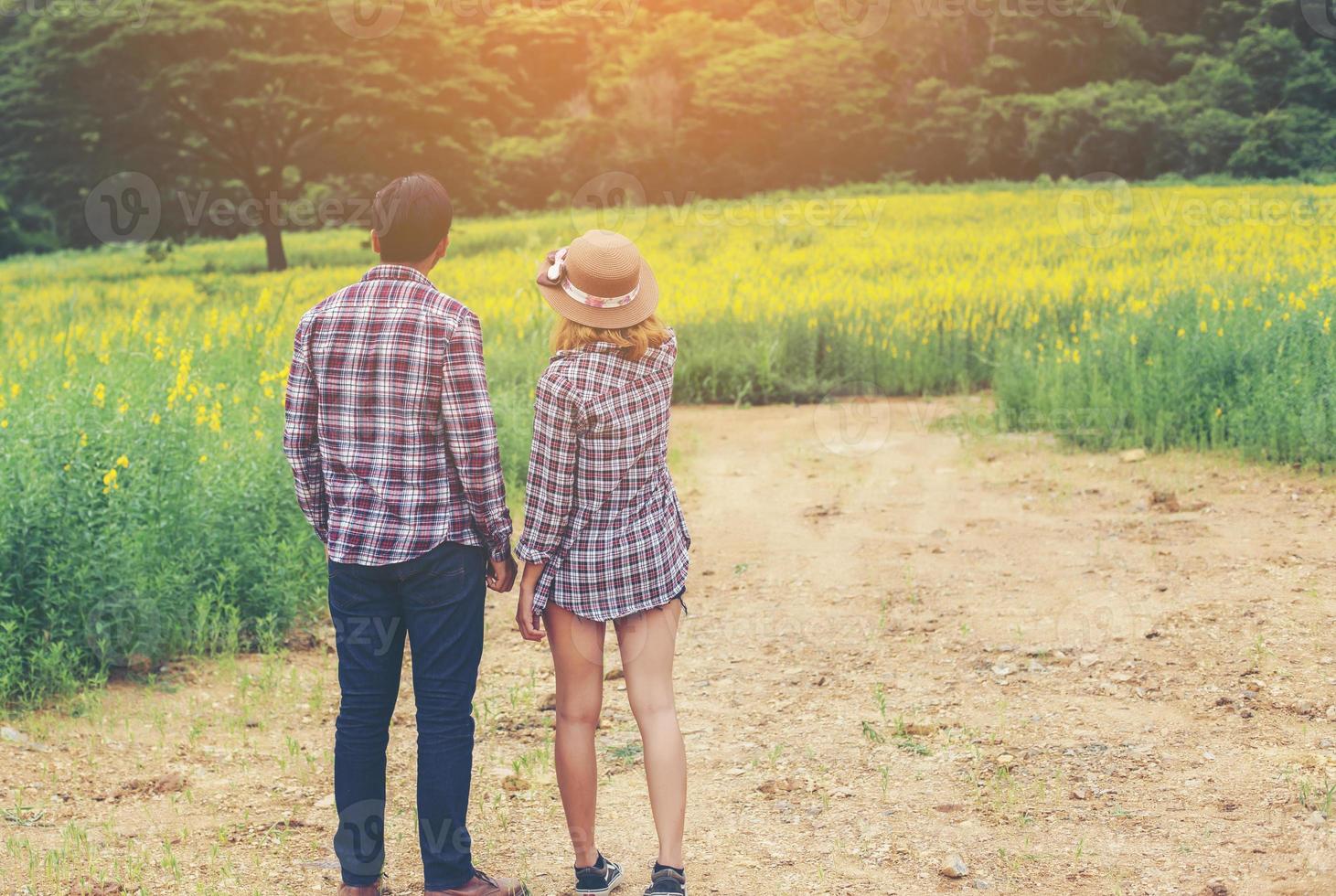 Young hipster couple relaxing in yellow flower field at summer. Enjoying with nature. photo