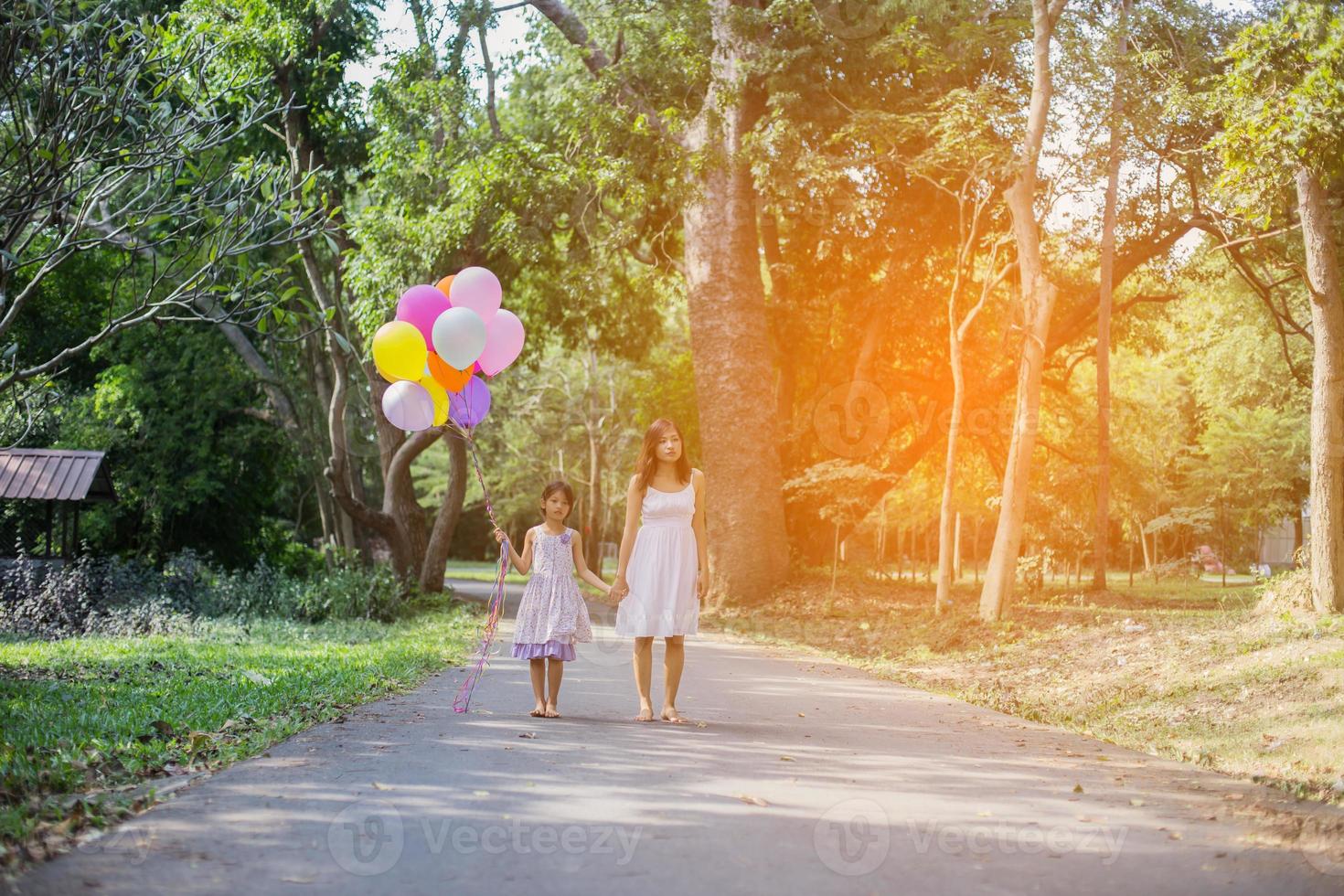 Cute little girl holding colorful balloons, running in the meadow against blue sky and clouds. photo