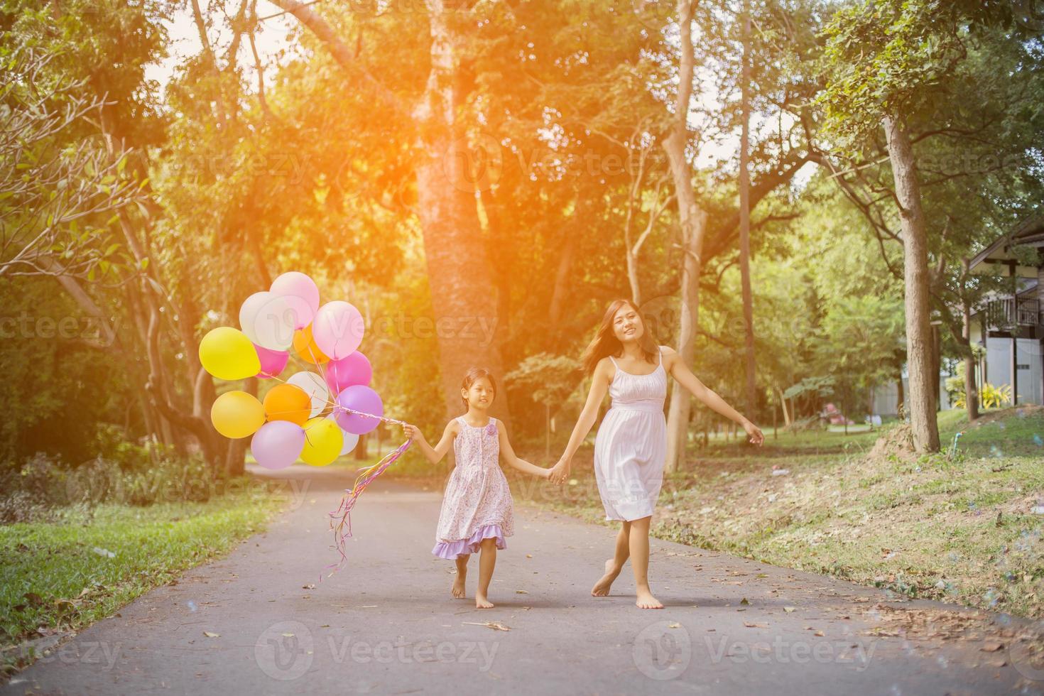 Cute little girl holding colorful balloons, running in the meadow against blue sky and clouds. photo