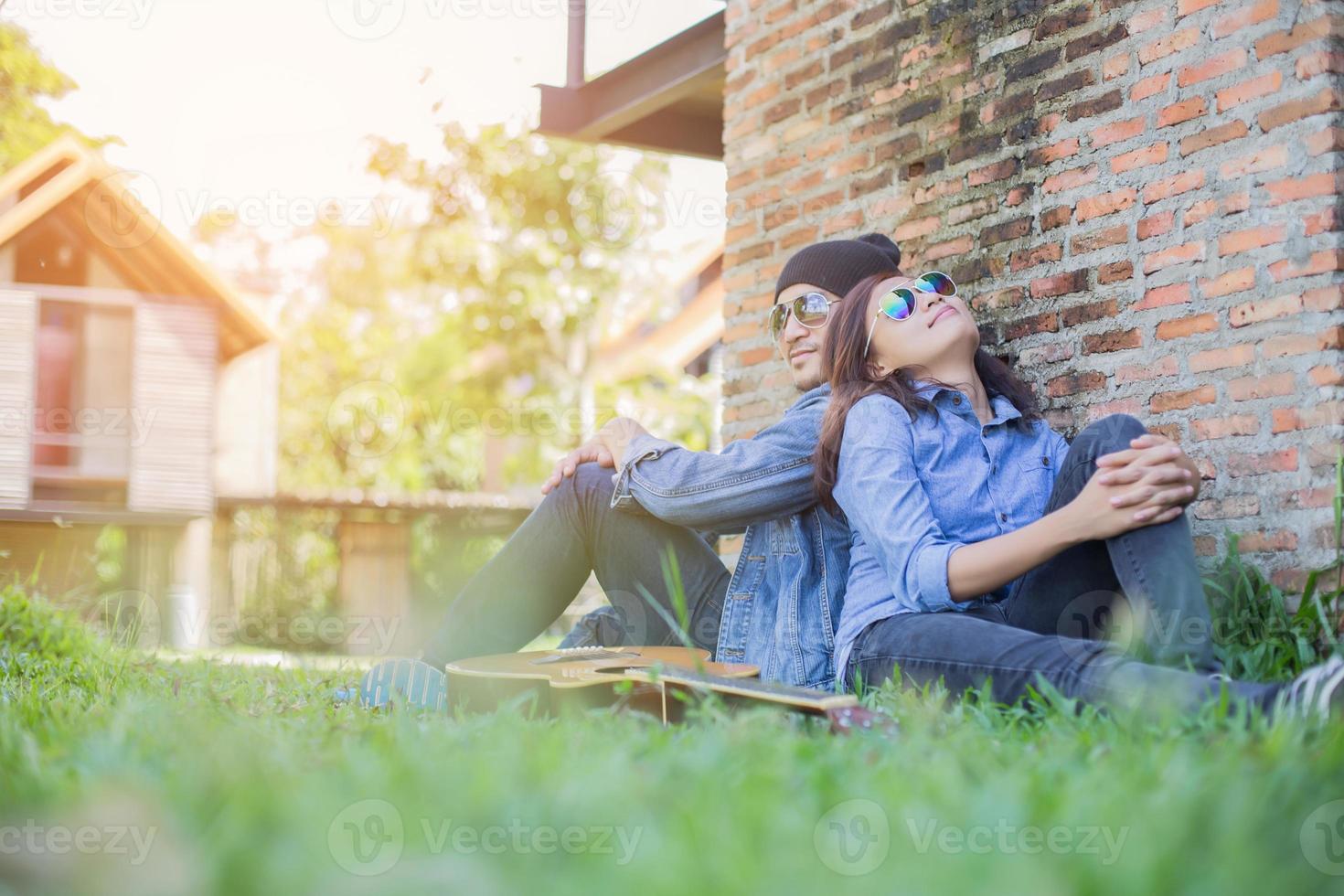 Hipster man playing guitar for his girlfriend outdoor against brick wall, enjoying together. photo