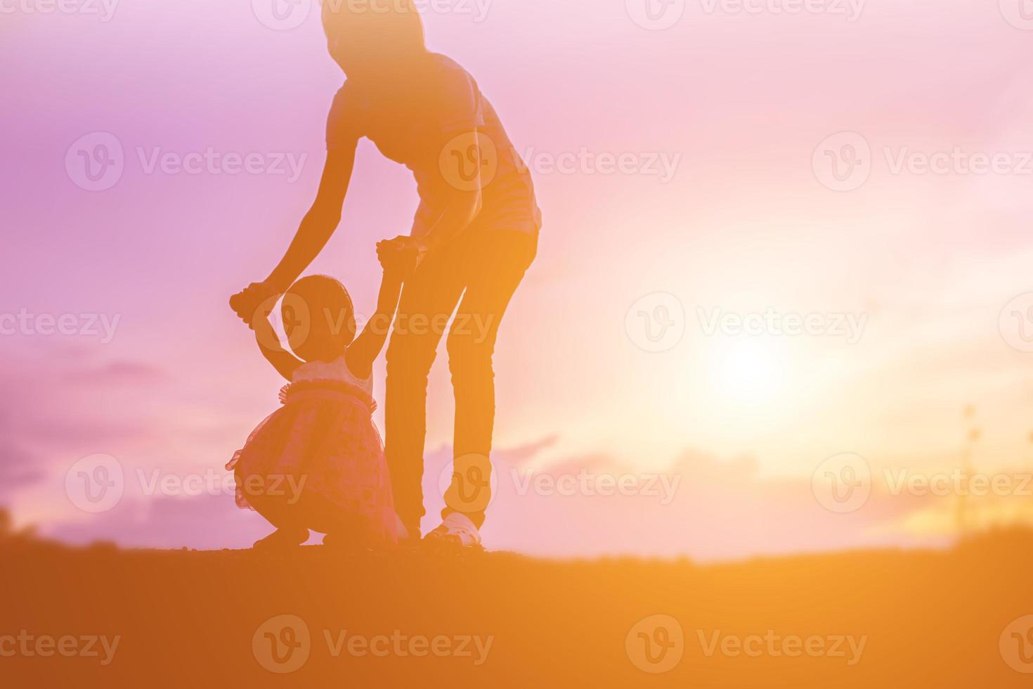 una silueta de una niña feliz los brazos de su madre amorosa para un abrazo, frente a la puesta de sol en el cielo en un día de verano. foto