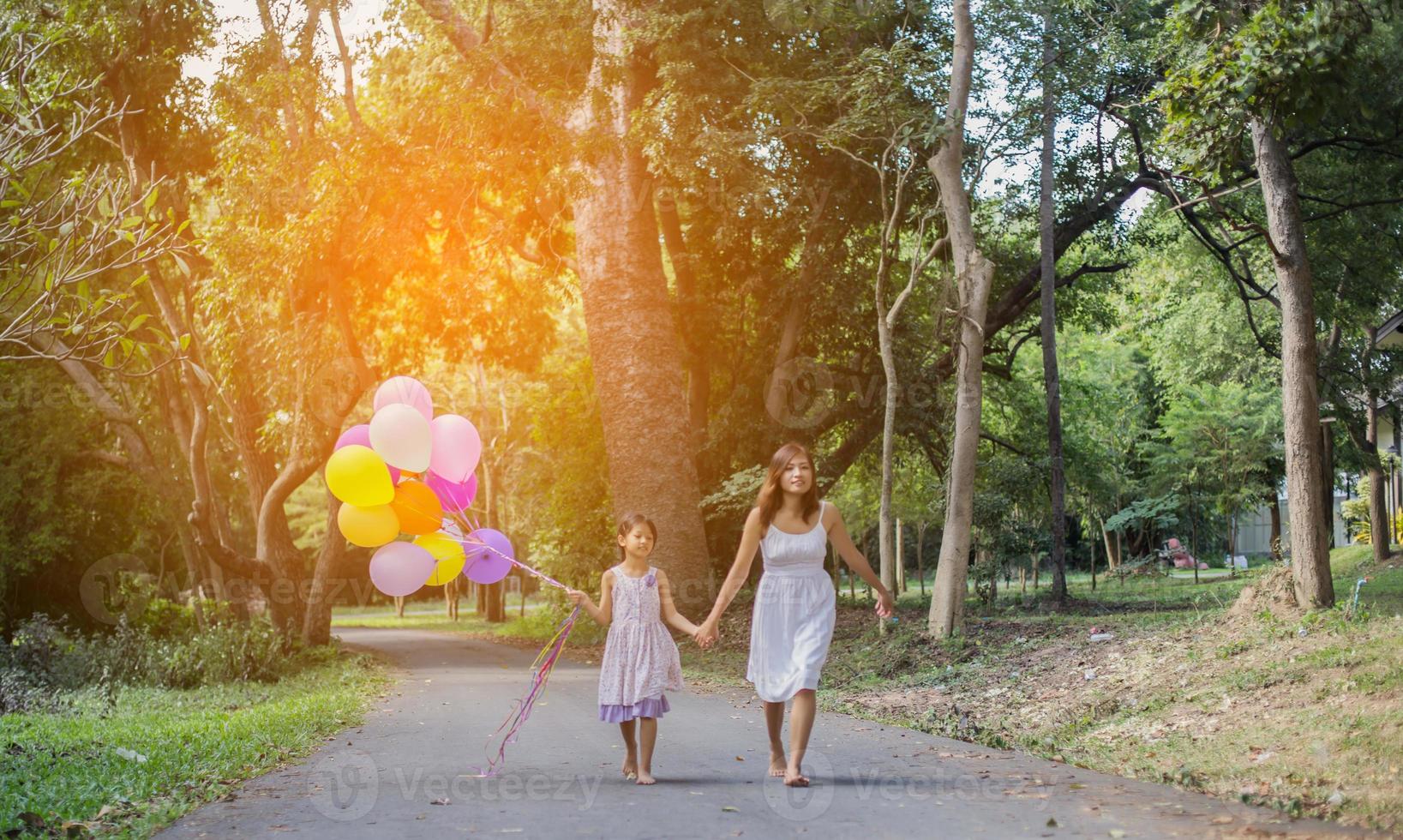 Cute little girl holding colorful balloons, running in the meadow against blue sky and clouds. photo