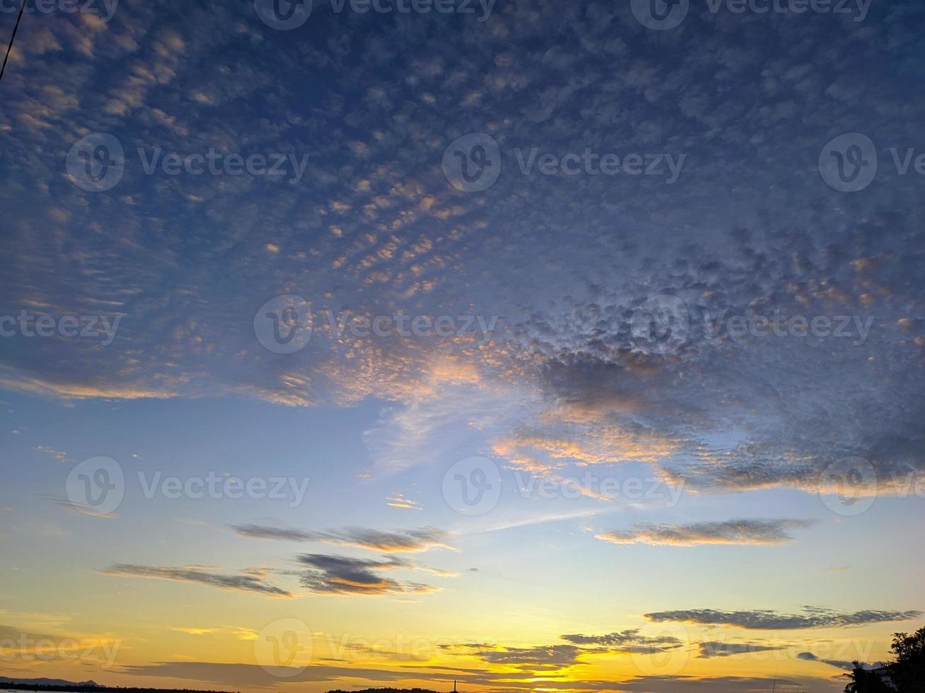 The blue sky in the evening beside the beach is dotted with white clouds and yellow light emitting from the sunset photo