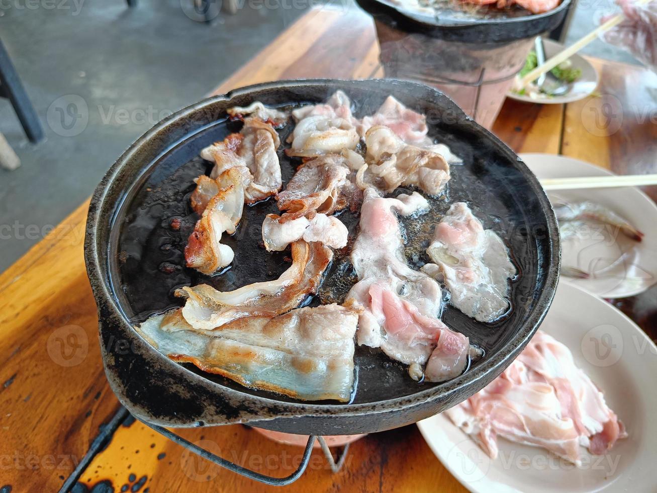 Grilled pork belly on a hot pan, on a wooden table photo