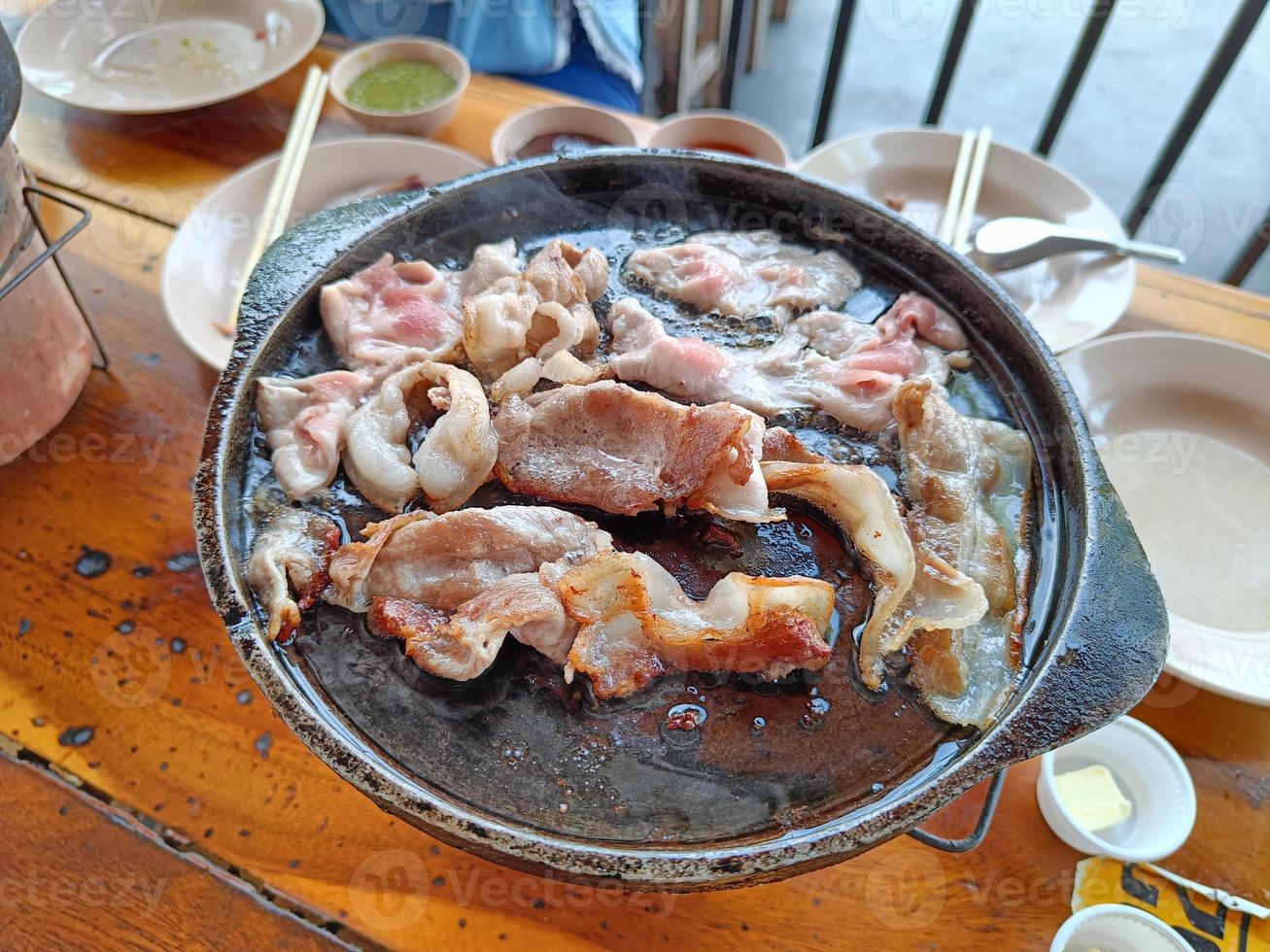 Grilled bacon on a hot pan, on a wooden table photo