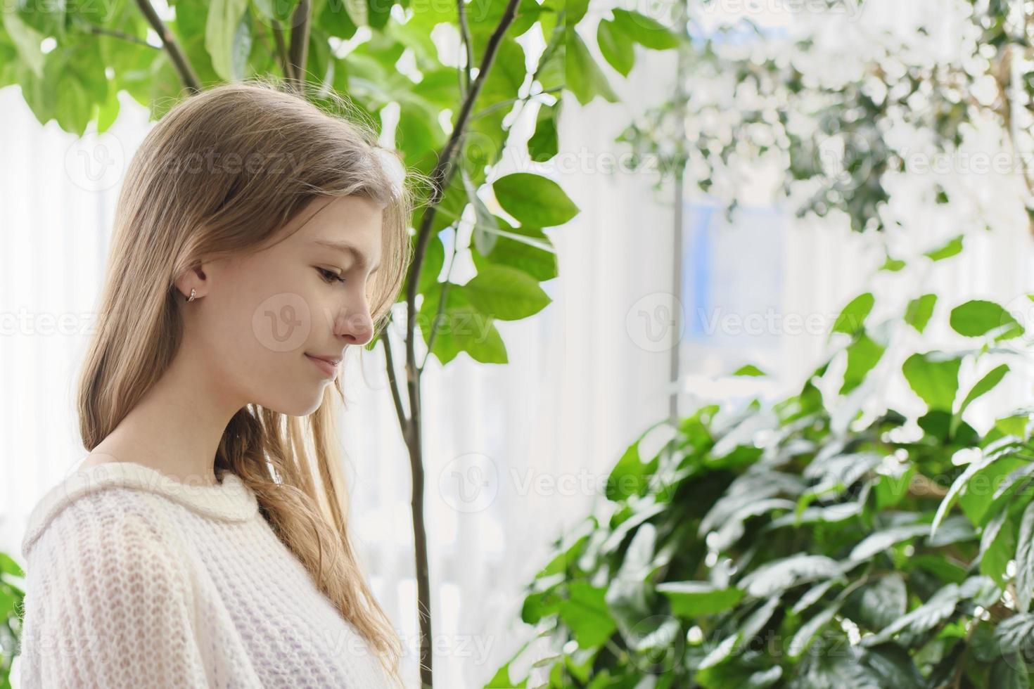 side portrait of a teenager girl in a modern house with lots of green plants on a background. generation z concept photo