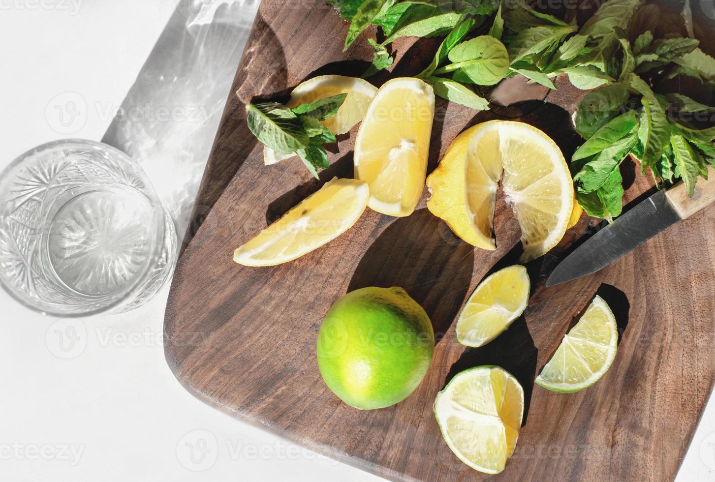 homemade mojito lemonade preparing. lemon and lime slices and fresh mint leaves on a cutting board. detox drinks for summer. photo