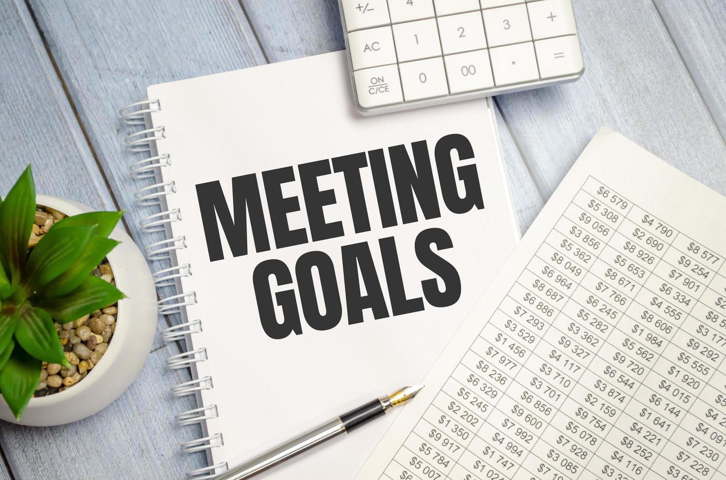 notebook over wood table background, focus on wooden blocks with letters making MEETING GOALS photo