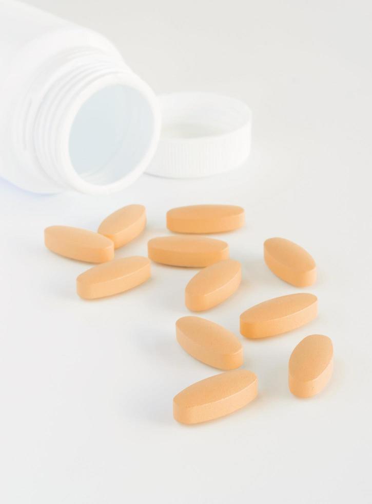 Orange pills and white bottle with lid on white background photo