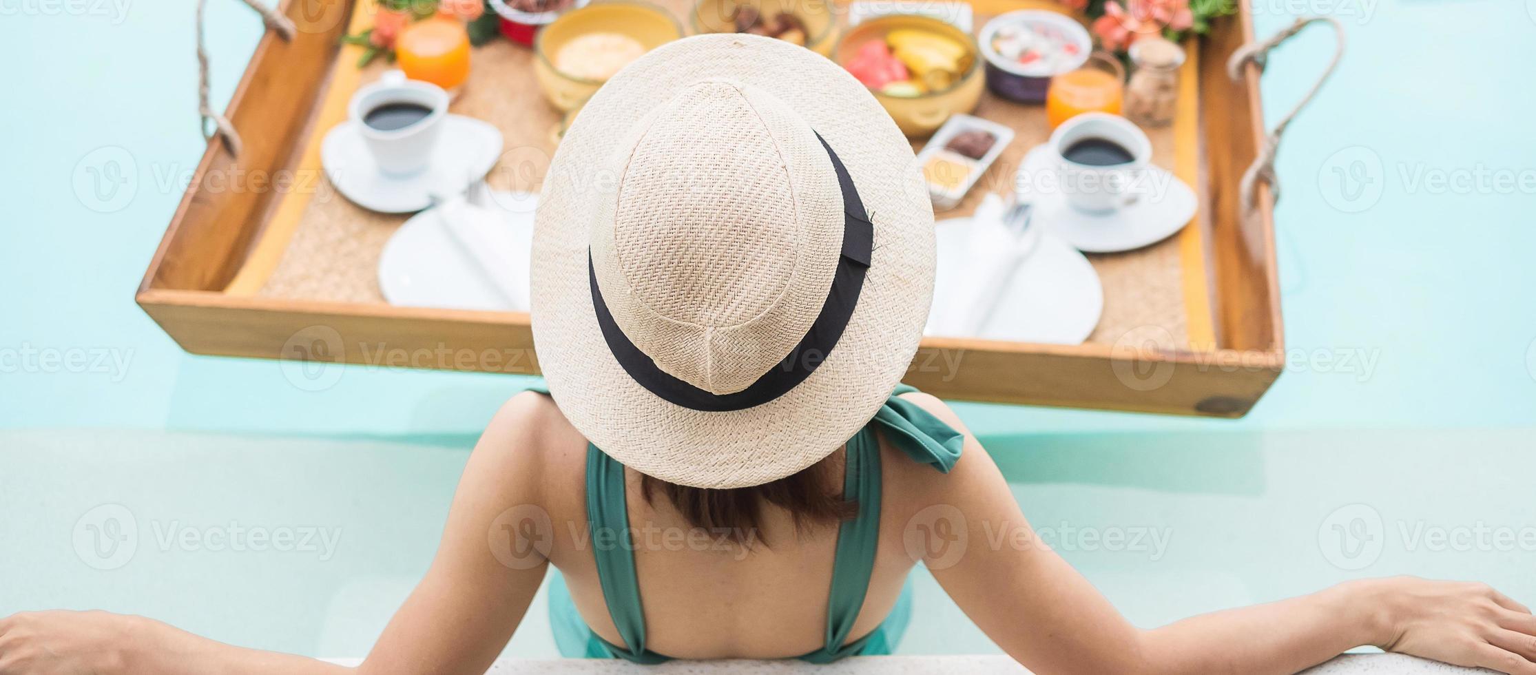 Happy young woman in green swimsuit having Floating Breakfast tray in luxury pool hotel, girl with hat enjoy in tropical resort. Relaxing, Exotic summer travel, holiday, vacation and tropical photo