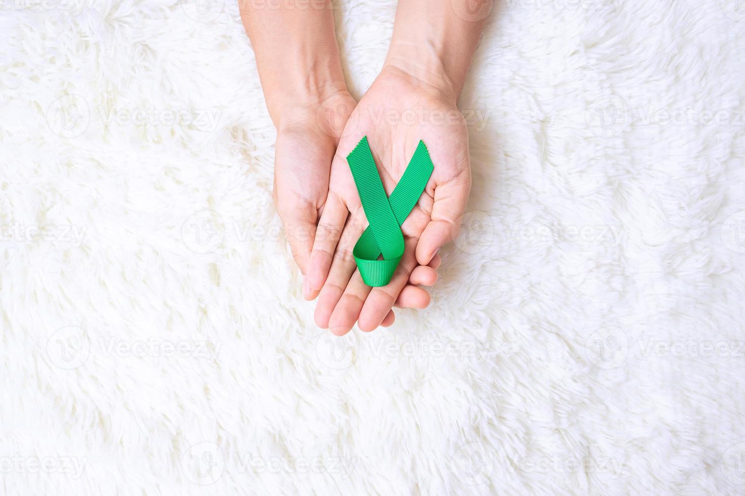 Hand holding green Ribbon for supporting people living and illness. Liver, Gallbladders bile duct, kidney Cancer and Lymphoma Awareness month concept photo