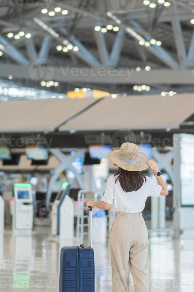 Young woman hand holding luggage handle before checking flight time in airport, Transport, insurance, travel and vacation concepts photo