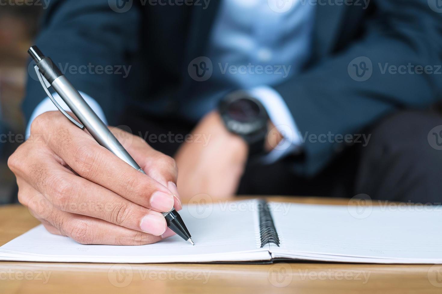 Businessman in suit writing something on notebook in office or cafe, hand of man holding pen with signature on paper report. business concepts photo