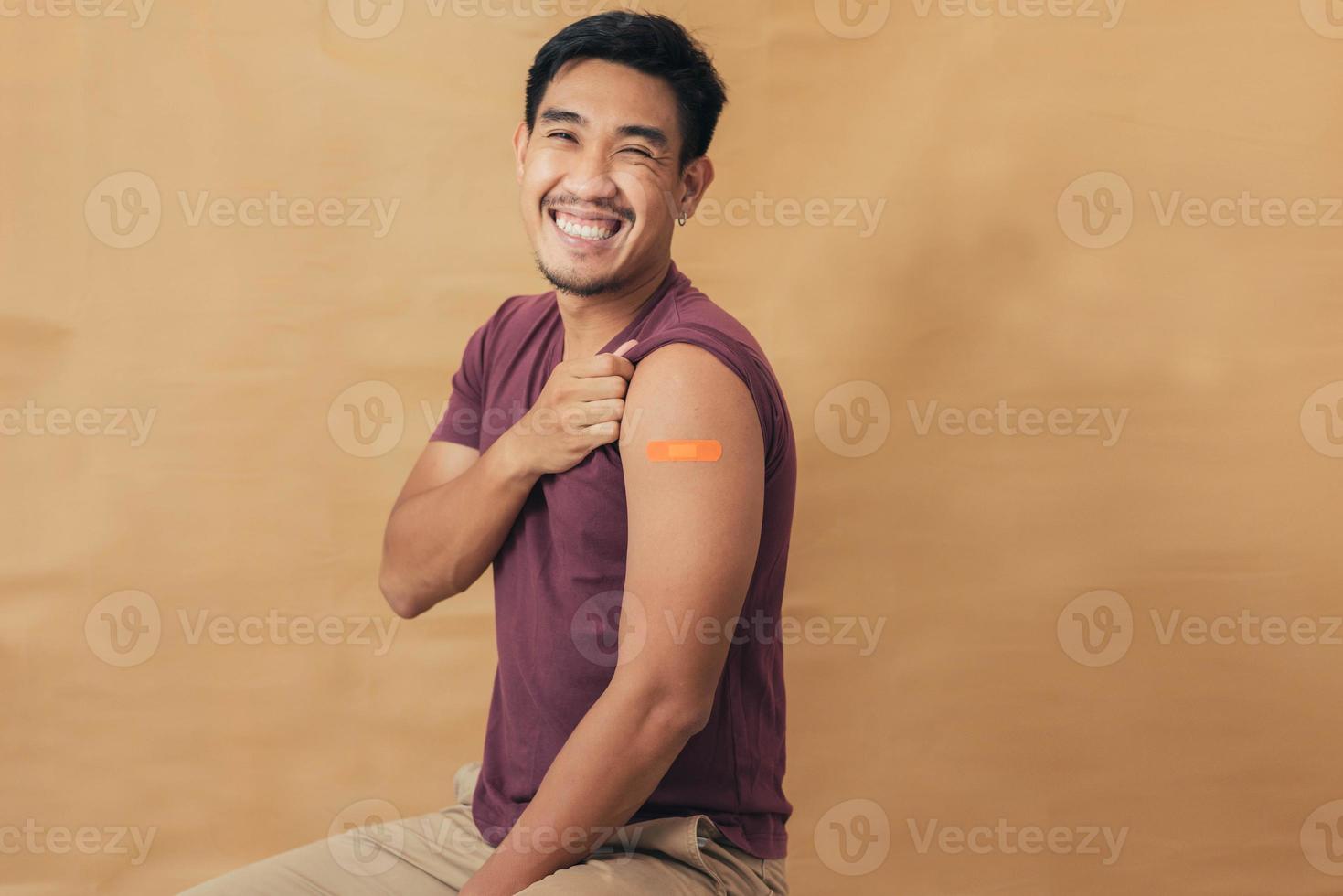 Asian man showing shoulders after getting a vaccine. Happy man showing arm with band-aids on after vaccine injection. photo