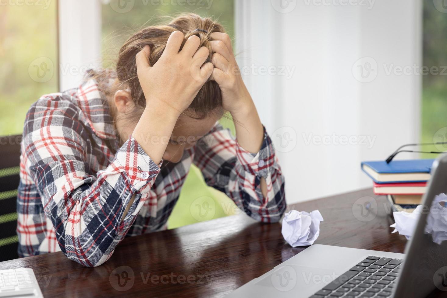 mujer de negocios con dolor de cabeza mientras trabaja con una computadora portátil. niña estresada y deprimida tocándose la cabeza, sintiendo dolor mientras se sienta en una mesa de madera, concepto de falla laboral foto