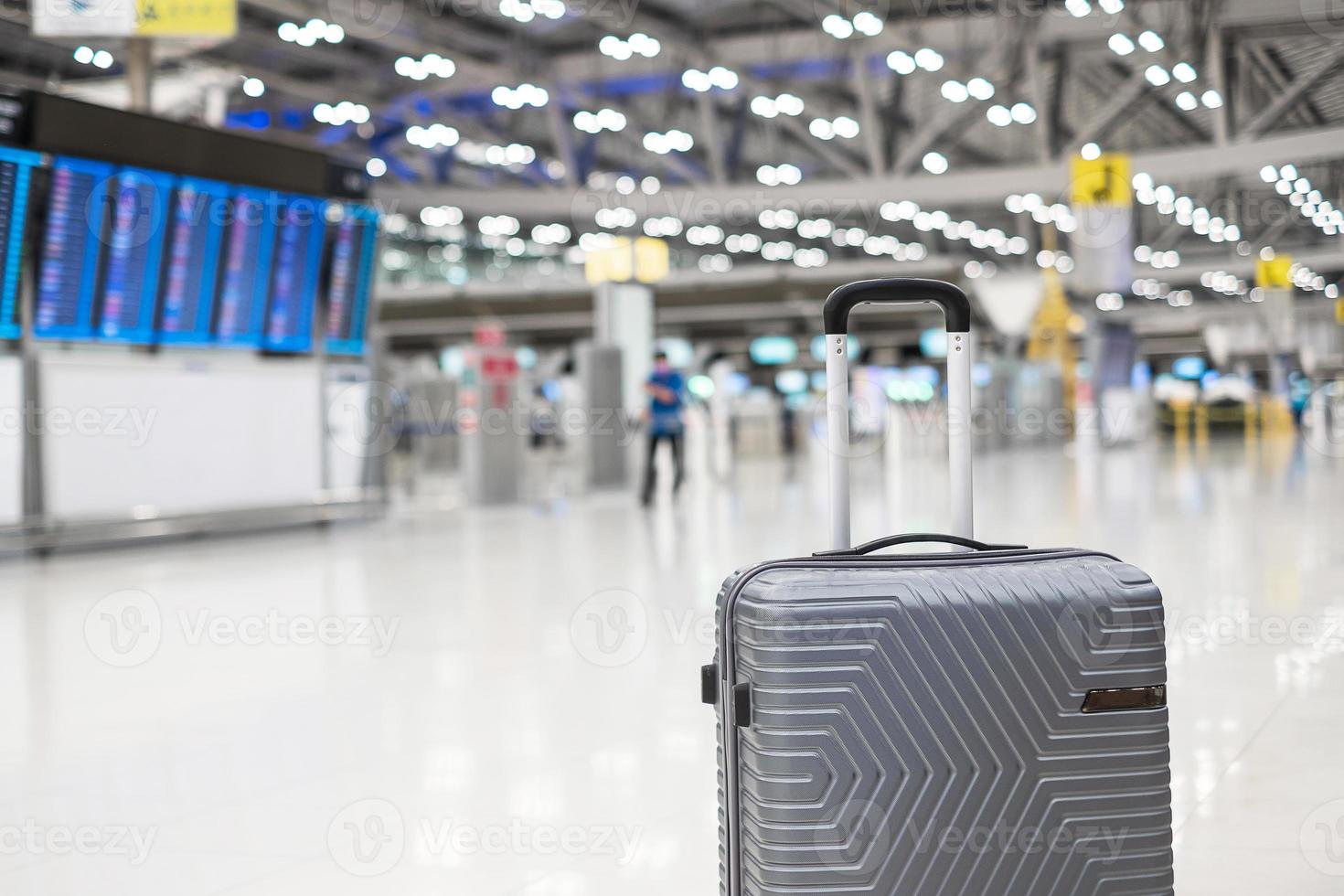 luggage bag in international airport terminal, trolley suitcase with information board in aerodrome background. Transport, insurance, travel and vacation concepts photo